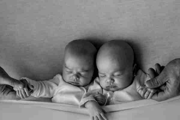 Heartwarming black and white photo of peaceful sleeping twin babies held by adult hands.